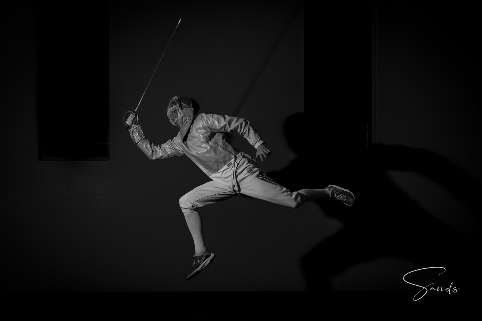 A KZN fencer mid-lunge in full fencing kit, captured in black and white