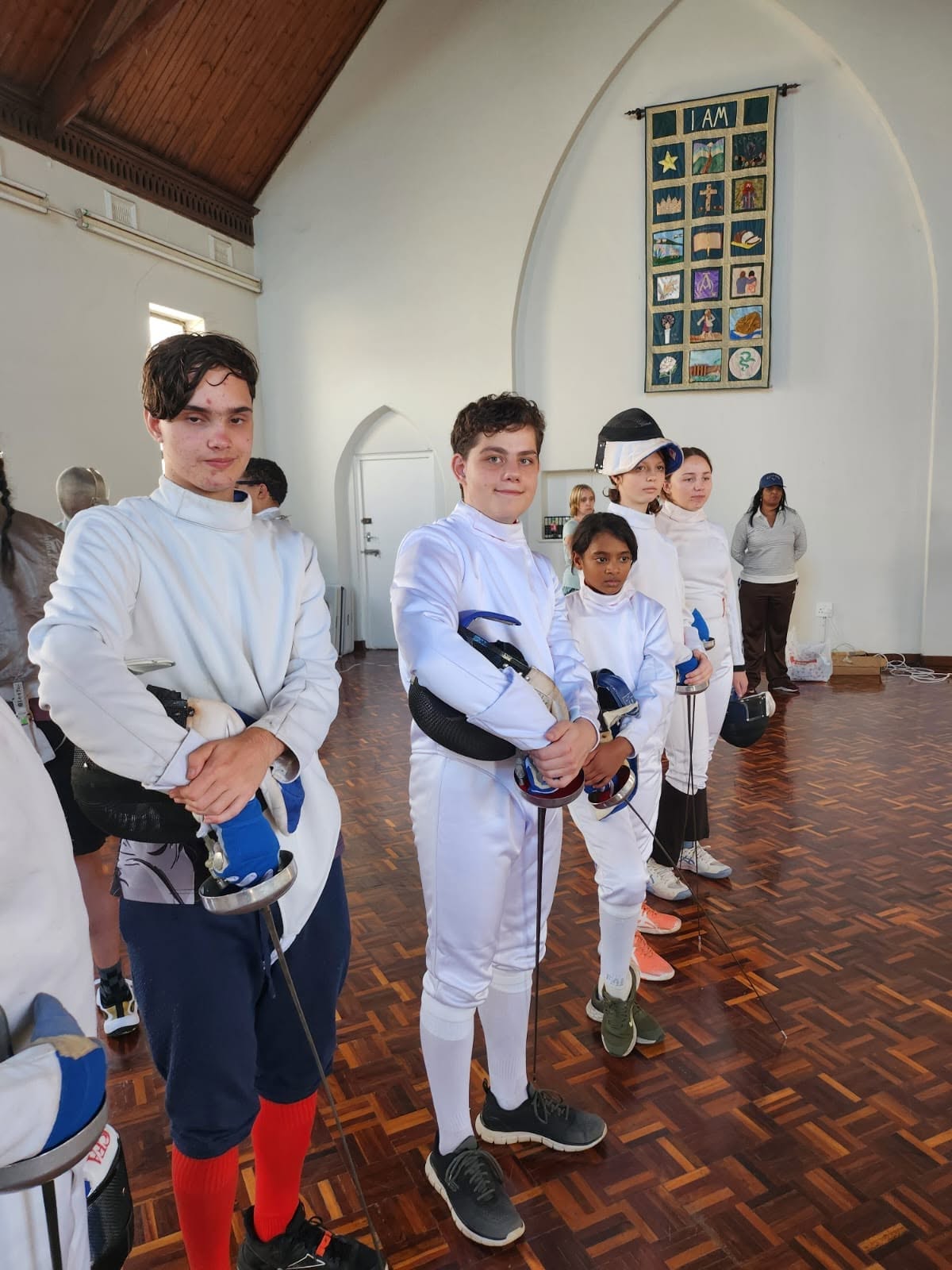 Young fencers in full kit standing in line, waiting for their bouts